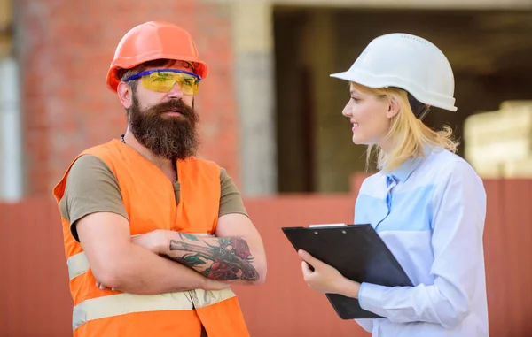 Vrouw inspecteur en bebaarde brute builder bespreken bouw vooruitgang. Bouw project inspecteren. Bouw website veiligheidsinspectie. Voortgang project bespreken. Inspecteur veiligheidsconcept — Stockfoto