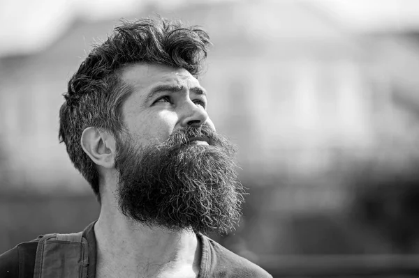 Hipster with beard and mustache on strict face looks at sky, urban background, defocused. Bearded guy enjoy sunny weather. Man with beard looks at sky on sunny day. Weather forecast concept