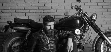Yenilikçi, vahşi Motorcu deri ceketli dalgın yüzündeki motosiklet yakın yerde oturamaz. Vahşi motorcu kavramı. Sakallı, motorcu motorlu bisiklet garaj, tuğla duvar arka plan yakınındaki deri ceketli adam