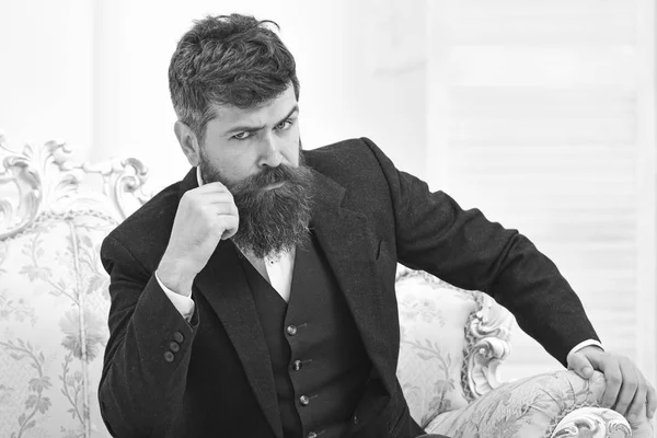 Concepto de estilo de vida Elite. Hombre con barba y bigote con traje clásico, se sienta en un sillón o sofá a la antigua. Macho atractivo y elegante en cara seria y expresión reflexiva —  Fotos de Stock