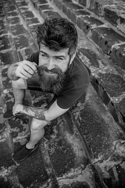 Macho avec barbe et moustache assis sur fond d'escalier en pierre. Hipster sur le visage joyeux relaxant en plein air. L'homme se repose, profite de la fraîcheur après la pluie. Concept après la pluie — Photo