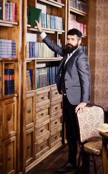 Bookcase and reading concept. Bearded man takes book from bookcase