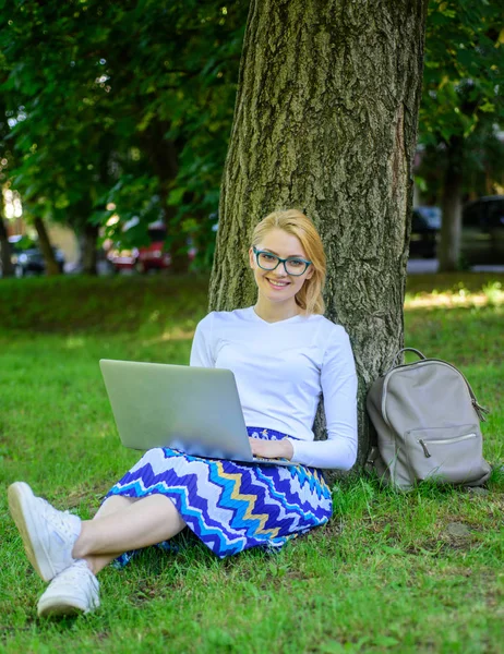 Wi-fi hálózati kapcsolat ingyenes hozzáférés. Lady szabadúszóként dolgozik a parkban. Nő laptop működik szabadtéri, park háttérrel. Lány ül fű sovány fa törzse notebook. Szabadúszó előnyt — Stock Fotó