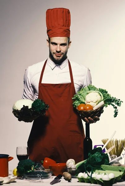 Chef in burgundy uniform holds baskets with cabbage and lettuce. — Stock Photo, Image