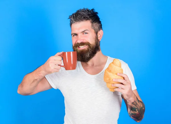Enjoy every sip of coffee. Perfect match. Man start morning with cup of coffee and fresh croissant. Bearded hipster enjoy breakfast drink coffee. Morning tradition concept. But first coffee