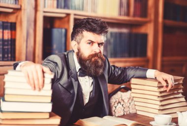 Adam masada çok kitap ile oturuyor..