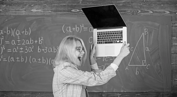 Teacher woman raising laptop above herself ready to destroy. Working conditions of teachers causes nervous disease. She needs pills to keep calm and mental health. Overstrain of the nervous system Stock Photo