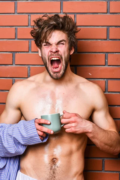 Mannen med skägg dricka kaffe tegel vägg bakgrund. Kille hålla te eller kaffe kopp. Idrottsman sömnig ansikte rufsig hår slitage badrock håll mugg. Macho sexig torso njuta av kaffe. Morgon kaffe konceptet — Stockfoto