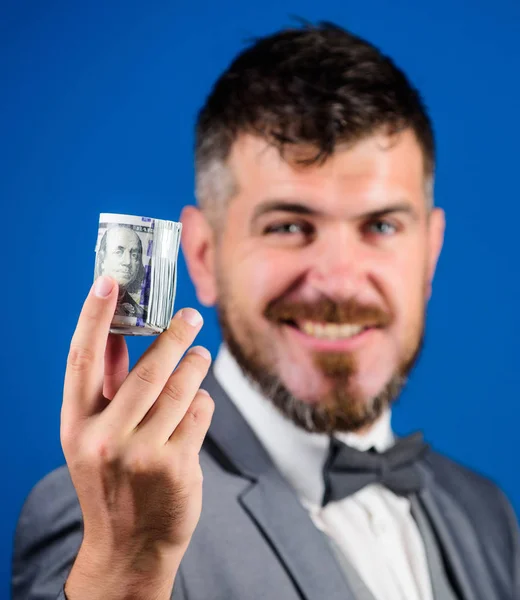 Hipster offer money blue background close up. Easy money concept. Rich businessman hold rolled money. Man bearded hipster hold rolled dollars banknotes. Guy formal suit offer bribe or purchase