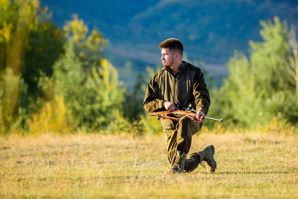 Homem a carregar espingarda de caça. Caça como passatempo masculino e lazer. Troféu de caça. Hunter roupas cáqui pronto para caçar segurar fundo montanhas arma. Caçador com rifle à procura de animais — Fotografia de Stock