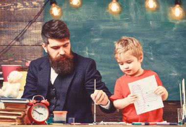 Baba oğluna suluboya nasıl kullanılır gösteriyor. Elinde çizim tutan sevimli bir çocuk. Yaratıcılık kavramı