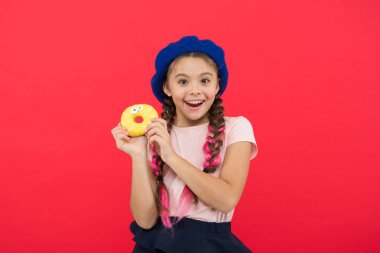 Kız tatlı çörek elinde kırmızı camlı arka plan tutun. Çocuk gülümseyen kız donut yemeye hazır. Şeker dükkanı ve ekmek kavramı. Pişmiş Donuts büyük fanlar çocuklar. Resist taze yapılmış çörek imkansız