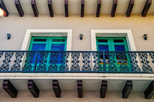 Balcony with decorative metal railing and two glass windows in green frames on plastered wall background in San Juan, Puerto Rico. Symmetry and urban geometry concept. Construction and renovation.