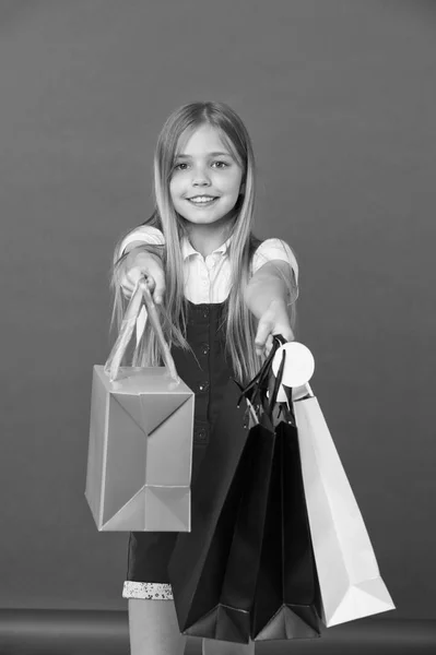 Chica sosteniendo coloridas bolsas de compras. Modelo con pelo largo y rubio sobre fondo violeta. Niño dando regalos en bolsas de papel, el estado de ánimo de vacaciones. Pequeño comprador gran gastador, moda y concepto de ventas —  Fotos de Stock