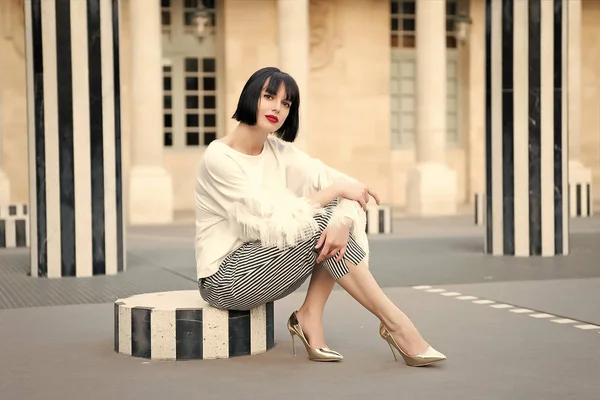 Woman with brunette hair sit at street stripped column.