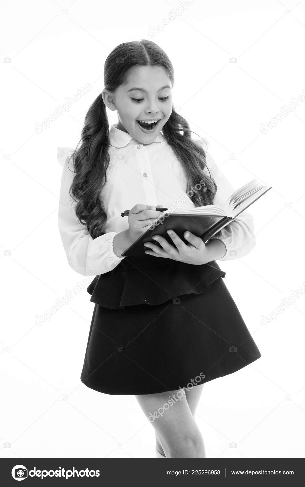 Маленький ребенок с удивленным взглядом изолирован на белом. Школьница с  длинными волосами держит книгу с ручкой. Девочка в школьной форме, обратно  в школу. Гений моды. Откройте книгу для жизни стоковое фото ©stetsik