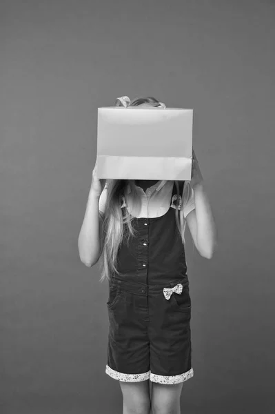 Blind of shopping. Kid holds package in front of face. Simple reminders how to shop smart. Girl cute teenager carries shopping bag. Kid bought clothing summer sale. Seasonal sale concept