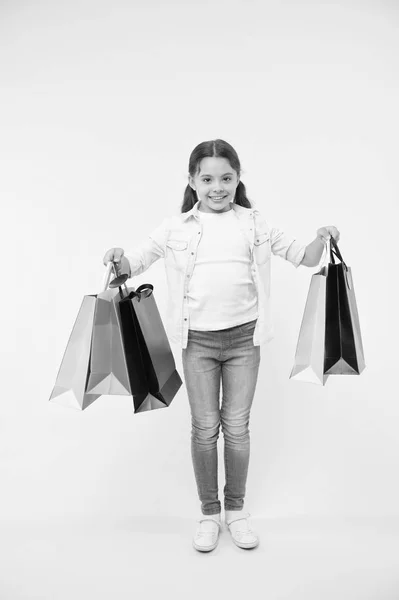 Kis segítője. Gyermek aranyos fashionista segít a csomagok hordoz egy vásárlás során. Kis üzlet eladó. Gyerek lány boldog mosolygó arc hordozza csomó csomagok sárga háttéren. Shopaholic lány szereti, vásárlás — Stock Fotó
