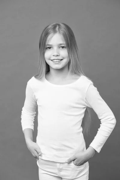 Lány hosszú szőke haj, test és kozmetikai koncepció. Gyerek visel fehér ruhát. Gyermek bájos mosollyal elszigetelt lila háttér. Divat-model új gyűjteménye ruházati márka reklám — Stock Fotó