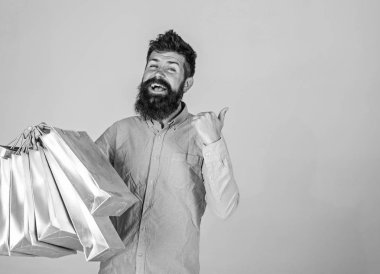 Sakal ve bıyık taşır grup alışveriş torbaları, gri arka planı olan adam. Adam alışveriş satış sezonu üzerinde boş yüzeyde işaret. Öneri kavramı. Satın almak için gülümseyen yüzü üzerinde hipster önerir