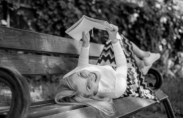 有趣的书。女士微笑的脸享受休息。女孩在户外看书, 同时在板凳上放松。女孩卧椅休闲与书, 绿色自然背景。妇女花闲暇与书 — 图库照片