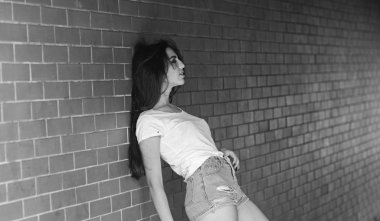 Kızı tuğla duvar arka plan poz rahat. Kadın duvara yalın verandada bekle. Birini bekliyor. Kız çekici esmer yeraltı geçidi veya metro takılmak rahatlatıcı. Metro kültür