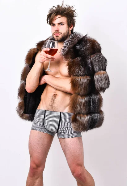 Moda y pathos. Riqueza y concepto de lujo. Chico atractivo rico posando abrigo de piel en cuerpo desnudo. Atleta rico disfrutar de su vida. Sexy soñoliento rico macho tousled pelo beber vino aislado en blanco — Foto de Stock