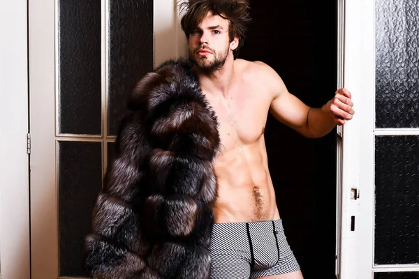 Chico atractivo posando abrigo de piel en cuerpo desnudo. Riqueza y concepto de lujo. Estilo de vida y bienestar de lujo. Símbolo de lujo. Sexy macho peluqueado saliendo por la puerta del dormitorio. Soltero rico amante — Foto de Stock