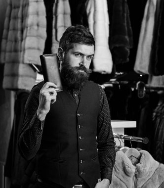 Adam düşünceli yüz cüzdan tutar. Maço cüzdan önünde lüks kürklü kıyafetleri ile. Lüks giyim kavramı. Sakal ve bıyık kürk dükkanda olan adam
