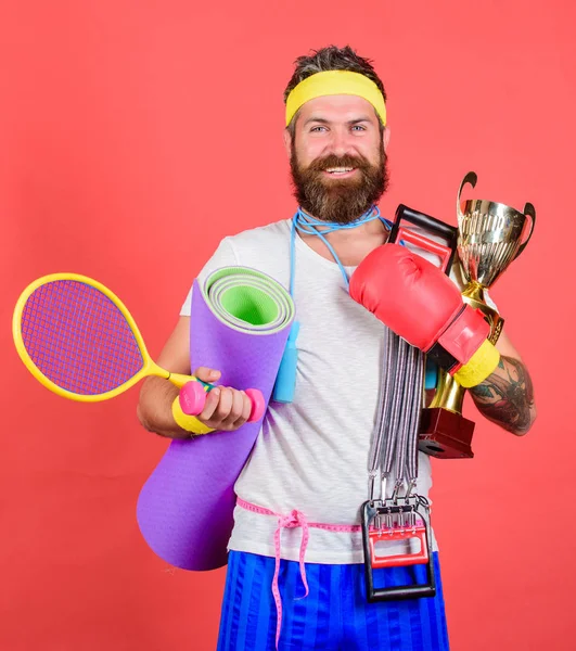 My goal is health. Man bearded athlete hold sport equipment jump rope fitness mat boxing glove expander racket and golden goblet. Sport shop assortment. Choose sport you like. Sport lifestyle concept