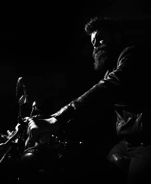 Хипстер, жестокий байкер в кожаной куртке на мотоцикле ночью, копия пространства. Человек с бородой, байкер в кожаной куртке сидит на мотоцикле в темноте, черный фон. Концепция ночных всадников — стоковое фото
