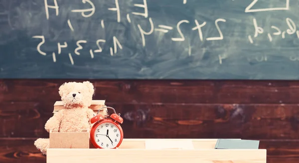教室里有黑板的背景。带有闹钟和泰迪熊的幼稚书桌。小学的概念。教室里有桌子和书, 还有抄写。小学教室的关闭 — 图库照片