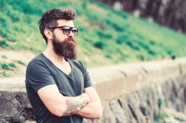 Berber ve stil kavramı. Sakal ve bıyık katı yüz, Doğa arka plan, defocused olan adam. Sakallı hippi açık havada duran ise kendinden emin görünüyor. Sakallı adam modern güneş gözlüğü takıyor