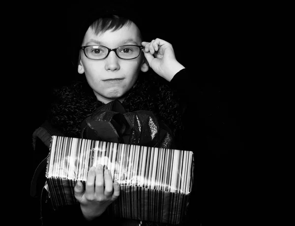 Small boy or cute nerd kid in glasses, hat and fashionable knitted scarf on black background holds colorful present box with red bo — Stock Photo, Image