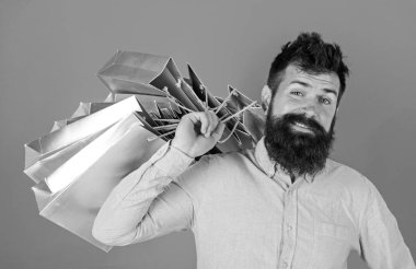 Sakal ve bıyık taşır alışveriş torbaları omuz, kırmızı zemin üzerine olan adam. Satış sezon indirimlerle alışveriş adam. Alışveriş kavramı. Mutlu yüz hipster bağımlısı alışveriş veya Alışverişkoliğin