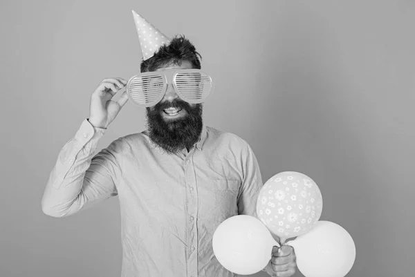 Happy bearded man in huge glasses posing with bright balloons, fun concept. Comedian with crazy look entertaining guests at special event. Perfomer with wild beard guiding contest at birthday party