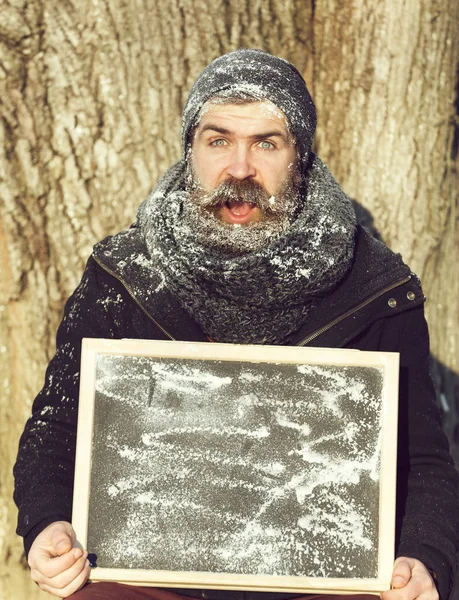 Skäggiga förvånad man hipster, med skägg och mustasch täckt med vit frost håller svarta tavlan vinterdag på naturlig bakgrund, kopia spac — Stockfoto