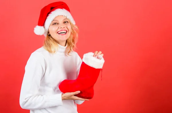 夫人在圣诞老人帽子举行圣诞礼物红色背景。圣诞长袜概念。女孩开朗的脸得到了礼物在圣诞袜子。检查圣诞长袜的内容。传统的寒假 — 图库照片