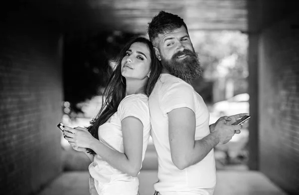 Send provocative message. Couple ignore real communication. Couple chatting smartphones. Girl and bearded man stand back to back porch or underground. Virtual cheating online. Suspect in cheating