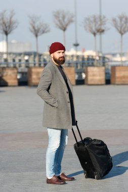 Tekerlekli bavul taşıyan sakallı bir hippi. Yolculuk başlasın. Bavullu gezgin havaalanı tren istasyonuna gitmek için bekliyor. Yola çıkmaya hazırız. Seyahat çantası taşı. İş gezisi