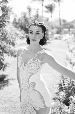 O mükemmel. Kız çekici lüks elbise aksesuarı. Lüks elbiseli kadın egzotik bahçe arka planında yürüyor. Makyaj yapan kadınlar şık dar elbiseler giyer. İşlemeli ve incili.