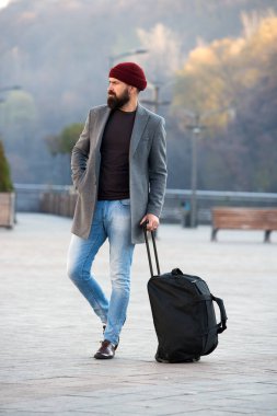 Ready to travel. Carry travel bag. Business trip. Man bearded hipster travel with big luggage bag on wheels. Let travel begin. Traveler with suitcase waiting transportation to airport railway station clipart