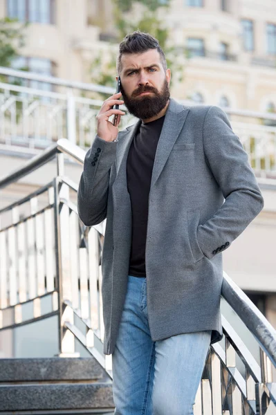 Stay in touch. Man bearded serious businessman hold mobile phone urban background. Hipster smartphone call partner. Man mobile call smartphone. Mobile call concept. Important mobile conversation.