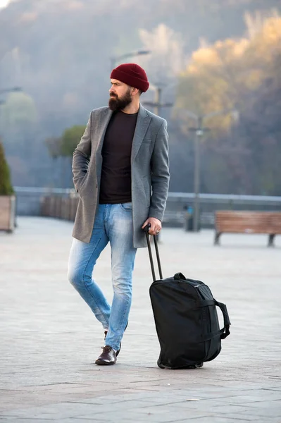 Ready to travel. Carry travel bag. Business trip. Man bearded hipster travel with big luggage bag on wheels. Let travel begin. Traveler with suitcase waiting transportation to airport railway station — Stock Photo, Image