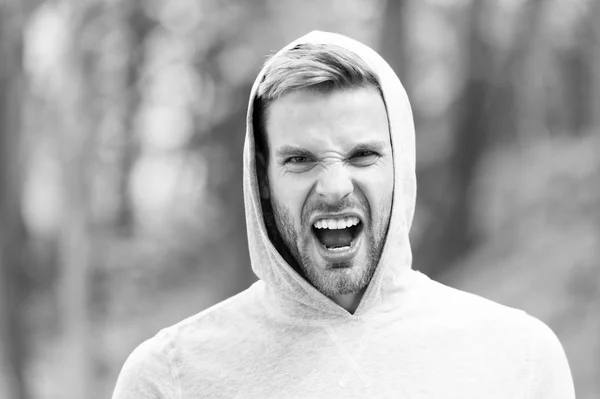 Man with bristle on shouting face, nature background, defocused. Skin care concept. Man with beard or unshaven guy looks handsome hooded. Guy bearded and attractive cares about his appearance — Stock Photo, Image