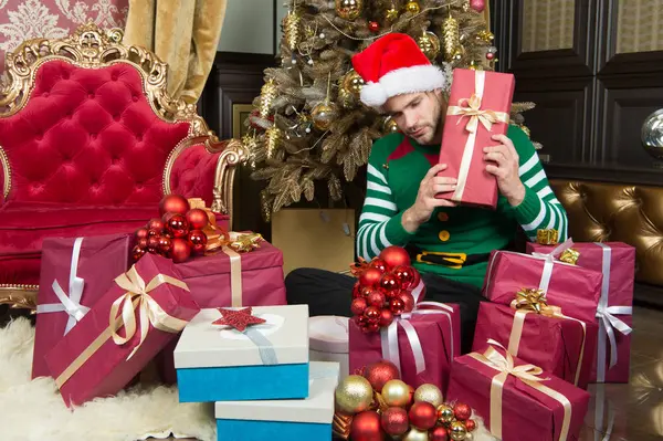 Aucun Noël n'est complet sans cadeaux. Heureux homme avec des boîtes-cadeaux de Noël. Un homme au chapeau de Père Noël tient des cadeaux de Noël. Il fête Noël à la maison. Livraison cadeaux de Noël — Photo