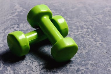 Gri dokuda parlak yeşil plastikten yapılmış dambıllar.