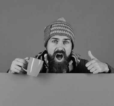 Sıcak şapkalı adam yeşil arka planda turuncu bardak tutuyor.