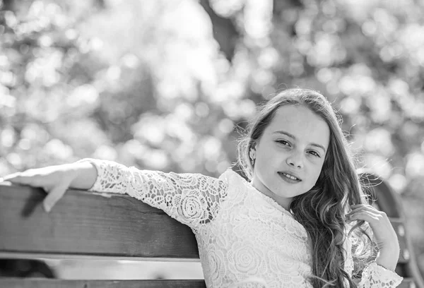 自然の美しさの概念。背景には、デフォーカスの桜の木のベンチに座っている笑顔の女の子。桜の近くの公園でリラックスした女の子。長い美しい髪のかわいい子は、日当たりの良い春の日をお楽しみください。 — ストック写真