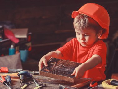 Kask Oluşturucu veya repairer, onarımı veya handcrafting olarak oynayan sevimli çocuk. Kavram handcrafting. Çocuk kör kütük çocuk tırnak ahşap pano içine. Yürümeye başlayan çocuk meşgul yüz oyunlarında evde atölye üzerinde